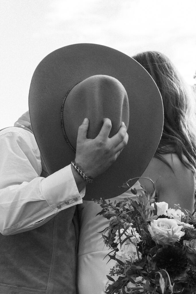 Groom kissing bride behind his cowboy hat